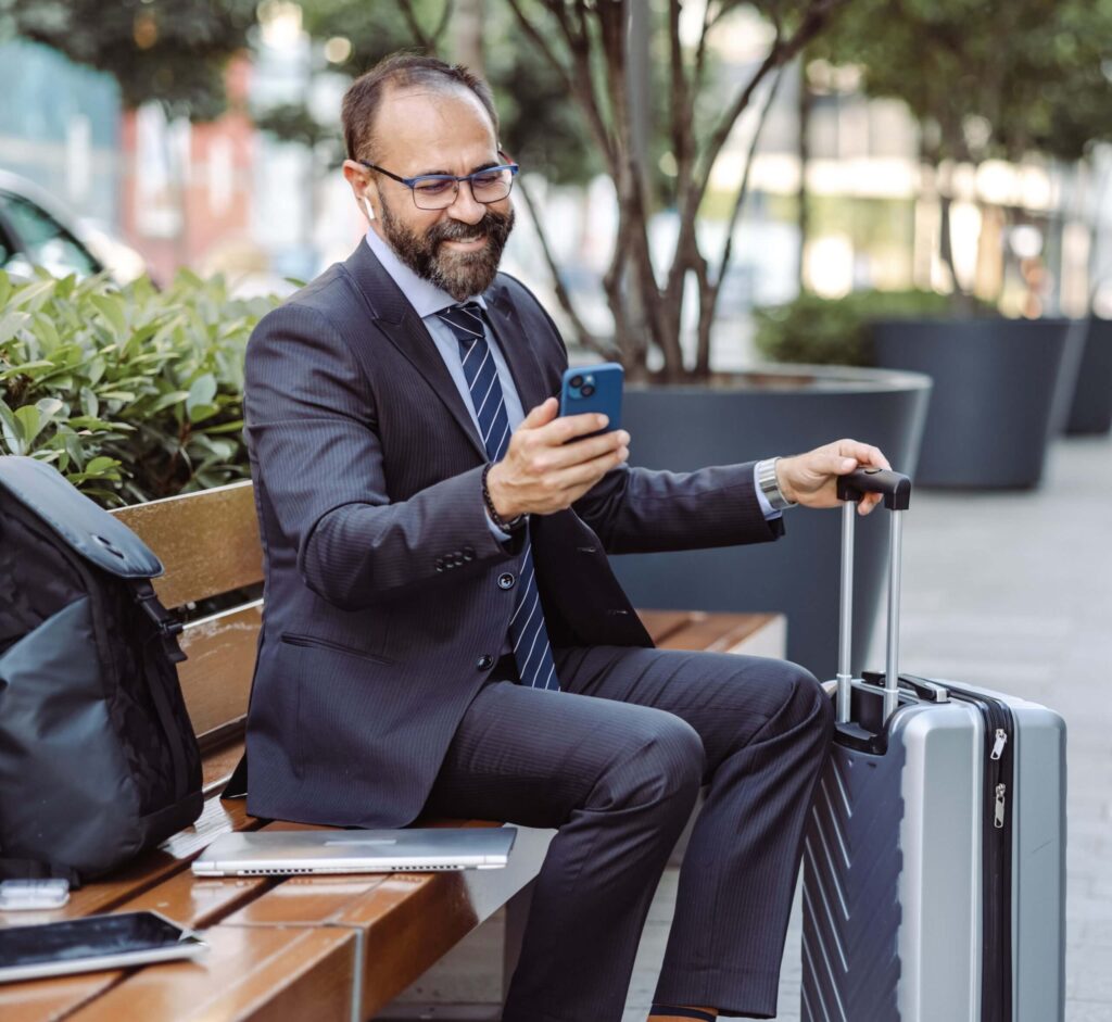 Mature businessman sitting on the bench, working on the laptop and using smart phone